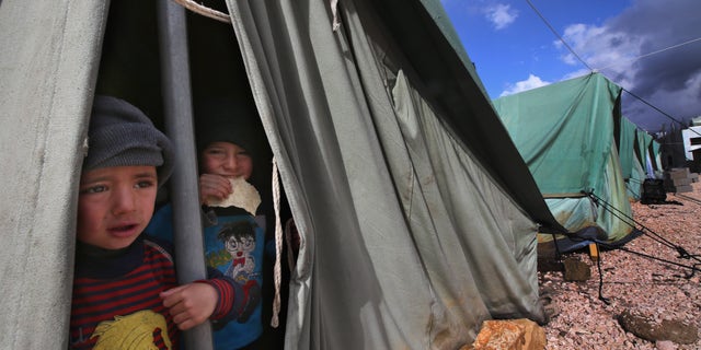 Syrian refugee boys look outside their tent, at a temporary refugee camp in the eastern Lebanese town of Marj near the border with Syria, Lebanon, Monday, Jan. 7, 2013. Syrian refugees worked on reinforcing their tents after they were flooded and some blown away by torrential rains and high winds. A heavy rainstorm coupled by snow on medium altitudes and high winds is hitting Lebanon causing material damage, flooding and trapping people in their cars. Particularly hard hit are thousands of Syrian refugees who fled to Lebanon, some of whom are staying in tents near the border with Syria. (AP Photo/Hussein Malla)