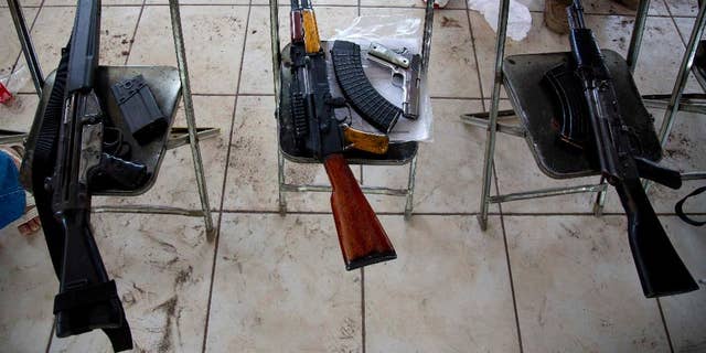 In this May 8, 2014 photo, weapons that belong to members of self-defense groups sit on chairs during a weapons registration operation in Apatzingan, Mexico. The self-defense members, identified by their white T-shirts, have registered thousands of weapons. But they’ve been allowed to keep them, even the large-caliber rifles that under Mexican law can only be used by the military. (AP Photo/Eduardo Verdugo)