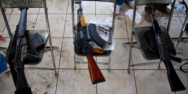 In this May 8, 2014 photo, weapons that belong to members of self-defense groups sit on chairs during a weapons registration operation in Apatzingan, Mexico. The self-defense members, identified by their white T-shirts, have registered thousands of weapons. But they’ve been allowed to keep them, even the large-caliber rifles that under Mexican law can only be used by the military. (AP Photo/Eduardo Verdugo)