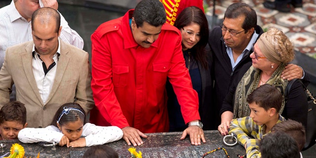 Venezuela's President Nicolas Maduro places his hands on the tomb of Venezuela's late President Hugo Chavez as he gathers with Chavez's family and government officials to mark the second anniversary of Chavez's death inside the 4F military museum in Caracas, Venezuela, Thursday, March 5, 2015. To the right of Maduro are first lady Cilia Flores, and Chavez's brother Adan. Chavez died of cancer at age 58 on March 5, 2013. (AP Photo/Ariana Cubillos)