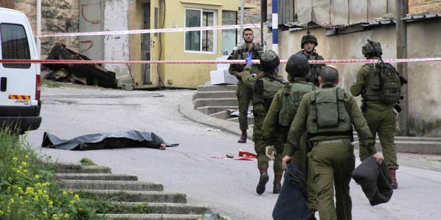 FILE - In this Thursday, March 24, 2016 file photo, Israeli soldiers stand near the body of a Palestinian who was shot and killed by a soldier while laying wounded on the ground after a stabbing attack in Hebron, West Bank. Israeli Prime Minister Benjamin Netanyahu defended the military Sunday, March 27, 2016 following uproar over footage of a soldier lethally shooting a Palestinian attacker who had already been shot and subdued. (AP Photo, File)