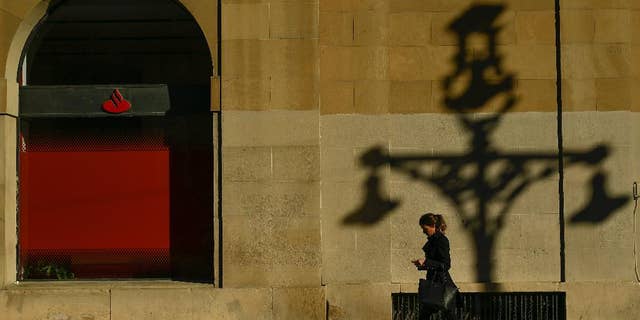 A woman walks past checking her personal phone beside a wall with the shadow of a street light, during an autumn day, in Pamplona northern Spain, Thursday, Dec. 1, 2016. (AP Photo/Alvaro Barrientos)