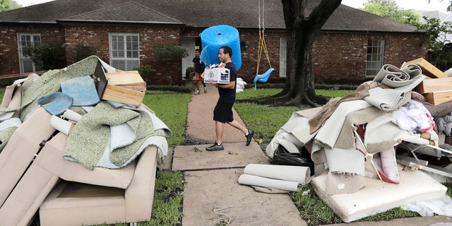 Michael Saghian carries a roll of bubble wrap and a box of sandwiches for workers helping remove items damaged by floodwaters from Tropical Storm Harvey from his home Wednesday, Aug. 30, 2017, in Houston