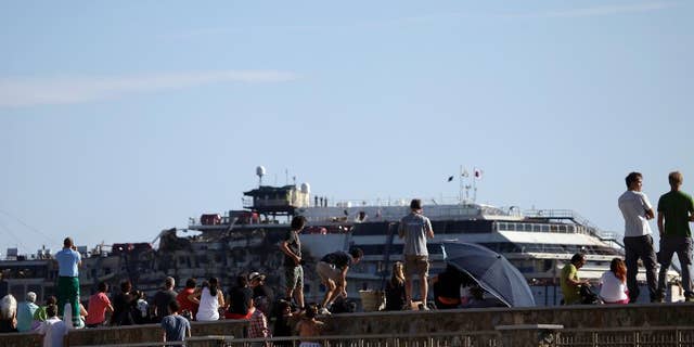 People gather to see the Costa Concordia cruise wreck being towed away from the tiny Tuscan island of Isola del Giglio, Italy, Wednesday, July 23, 2014.  After more than two years since it slammed into a reef along the coastline of Isola del Giglio the wreck has begun its last journey, to the Italian port of Genoa, where it will be scrapped. 32 people died in the incident. (AP Photo/Gregorio Borgia)