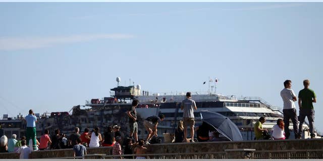 People gather to see the Costa Concordia cruise wreck being towed away from the tiny Tuscan island of Isola del Giglio, Italy, Wednesday, July 23, 2014. After more than two years since it slammed into a reef along the coastline of Isola del Giglio the wreck has begun its last journey, to the Italian port of Genoa, where it will be scrapped. 32 people died in the incident. (AP Photo/Gregorio Borgia)