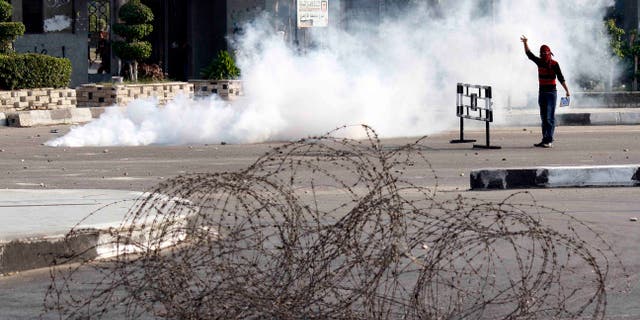 A masked protester stands in a cloud of tear gas during clashes with security forces dispersing several hundred pro- ousted President Mohammed Morsi university students who were rallying near Rabaah el-Adawiya, in eastern Cairo, Egypt, Monday, Oct. 28, 2013. As the protest got underway, army troops and police backed by armored vehicles blocked off the road leading to the site, creating a tense stand-off that lasted hours. By late afternoon, the students retreated to their campus, while pelting security forces with rocks.(AP Photo/Said Hamdy)