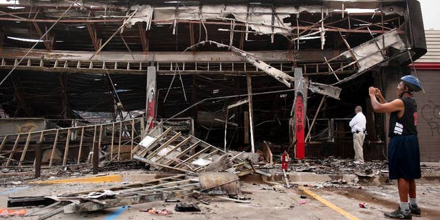 Aug. 11, 2014: Passers-by and media take a closer look at the burned-out shell of the QuikTrip gas station torched during the violence that erupted in Ferguson, Mo. overnight following a candle-light memorial for 18-year-old shooting victim Michael Brown.