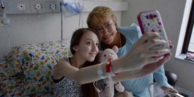 In this photo released by Chile's presidential press office, President Michelle Bachelet, right, poses for a selfie with Valentina Maureira, who suffers from cystic fibrosis, at a hospital in Santiago, Chile, Saturday, Feb. 28, 2015. Maureira posted a video on the web asking a meeting with Bachelet to allow her to "sleep for ever". (AP Photo/Chile's presidential press office