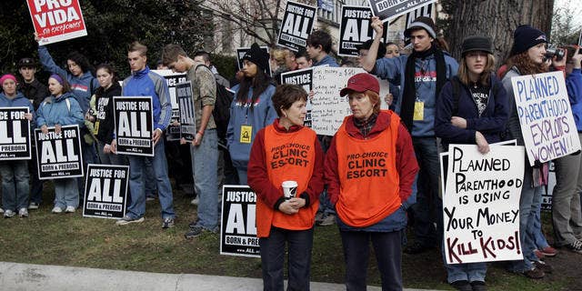 FILE: Planned Parenthood clinic escorts, in orange, stand in front of a group of anti-abortion protestors outside the Planned Parenthood clinic in Washington.