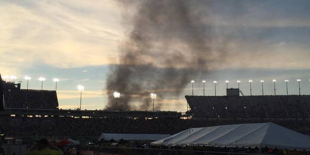 Smoke rises over the main grandstand from a vehicle fire in the platinum parking lot at the NASCAR Sprint Cup Series auto race at Kentucky Speedway, Saturday, July 9, 2016 in Sparta, Ky. (AP Photo/Gary Graves)