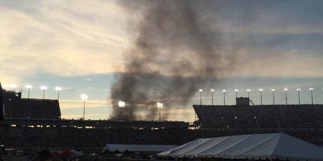 Smoke rises over the main grandstand from a vehicle fire in the platinum parking lot at the NASCAR Sprint Cup Series auto race at Kentucky Speedway, Saturday, July 9, 2016 in Sparta, Ky. (AP Photo/Gary Graves)