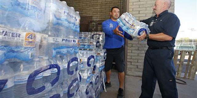 Glendale Fire Department firefighter Chris Greene, right, gets a case of water from service worker Edi Marroquin, left, from the dozens of cases of water at the Glendale Fire Department Resource Center as they prepare for the record-setting heat predicted for the weekend Thursday, June 16, 2016, in Glendale, Ariz. (Associated Press)