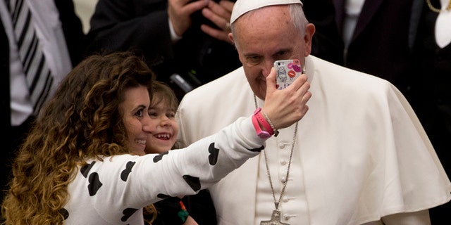 A woman and a child take a selfie photo with Pope Francis, right, during his weekly general audience in the Paul VI hall at the Vatican, Wednesday, Jan. 21, 2015. Pope Francis is praising big families after saying Catholics don't have to breed "like rabbits." He says big families are a gift and don't cause poverty in the developing world, and that the real cause of poverty is an unjust economic system that idolizes money over people. (AP Photo/Andrew Medichini)