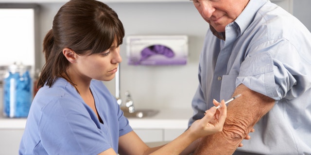 Doctor Giving Male Patient Injection In Hospital Room