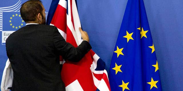 FILE- In this Oct. 15, 2015 file photo, a member of protocol adjusts the British and EU flags at EU headquarters in Brussels. As Britain prepares to vote whether to leave or stay in the European Union on June 23, 2016, goodwill between the continent and the island nation is fraying on both sides. (AP Photo/Virginia Mayo, File)