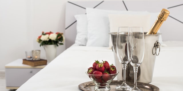 Champagne in bed in a hotel room, ice bucket, glasses and fruits on white linen