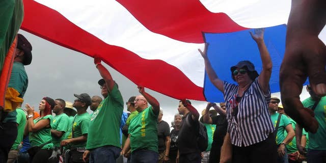 People carry a large Puerto Rican flag as they protest looming austerity measures amid an economic crisis and demand an audit on the island's debt to identify those responsible, in San Juan, Puerto Rico, Monday, May 1, 2017. Puerto Rico is preparing to cut public employee benefits, increase tax revenue, hike water rates and privatize government operations, among other things. (AP Photo/Danica Coto)