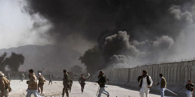 In this Feb. 22, 2012 file photo, protestors run as smoke rises from burning trucks during an anti-U.S. demonstration at a NATO military base in Jalalabad east of Kabul, Afghanistan.