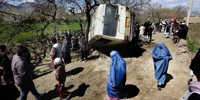 April 11, 2016: Afghan women walk past a damaged bus after a roadside bomb explosion on the outskirts of Kabul.