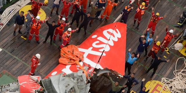 Jan. 10, 2015: Rescuers wave at an Indonesian Air Force helicopter near portion of AirAsia Flight 8501 after it was recovered from the sea floor on the deck of a rescue ship on the Java Sea