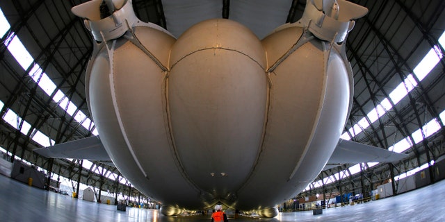 A worker stands under the Airlander 10 hybrid airship during its unveiling in Cardington, Britain March 21, 2016. (REUTERS/Darren Staples)
