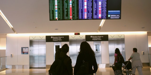 Airline passengers look at a flight status board at San Francisco International Airport in San Francisco