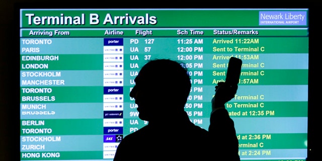 In this Wednesday, Nov. 27, 2013, file photo, a person points to a screen with an airplane travel list while holding up a phone at Newark Liberty International Airport, in Newark, N.J.