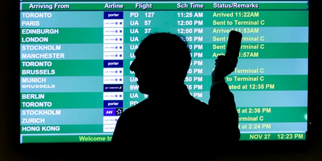 In this Wednesday, Nov. 27, 2013, file photo, a person points to a screen with an airplane travel list while holding up a phone at Newark Liberty International Airport, in Newark, N.J.