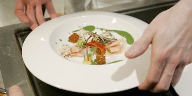 Chef Grant Achatz places a dish on a server's tray at Alinea in Chicago.