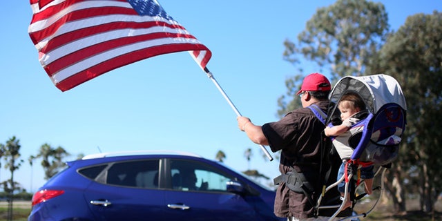 Demonstrator Steven Morales with his son Steven Jr. waves an American flag for motorists in support of President elect Donald Trump outside of Camp Pendleton in Oceanside, California, U.S. November 11, 2016. REUTERS/Sandy Huffaker - RTX2TA95