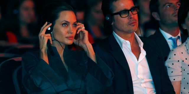 Actress and campaigner Angelina Jolie and her partner Brad Pitt wear headphones to listen to a translation during a global summit on ending sexual violence in conflict, at the ExCel Centre in London June 13, 2014. REUTERS/Luke MacGregor (BRITAIN - Tags: POLITICS ENTERTAINMENT) - RTR3TMBJ