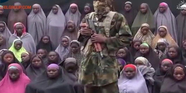 An alleged Boko Haram soldier stands in front of a group of girls alleged to be some of the 276 abducted Chibok schoolgirls held since April 2014, in an unknown location, in video distributed in August 2016.