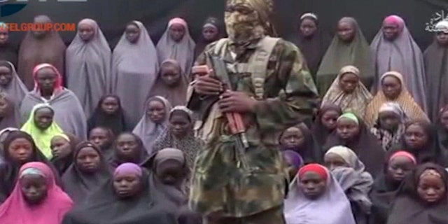 An alleged Boko Haram soldier stands in front of a group of girls alleged to be some of the 276 abducted Chibok schoolgirls held since April 2014, in an unknown location, in video distributed in August 2016.