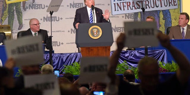 Protesters hold up signs as President Donald Trump speaks at the 2017 North America's Building Trades Unions National Legislative Conference in Washington, Tuesday, April 4, 2017. (AP Photo/Susan Walsh)