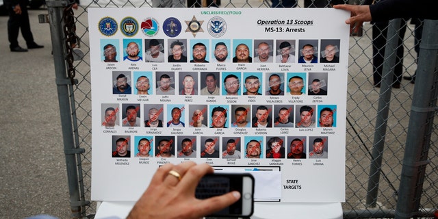 A reporter uses his smartphone to photograph a board showing images of MS-13 gang members during a news conference Wednesday, May 17, 2017, in Los Angeles. Hundreds of federal and local law enforcement fanned out across Los Angeles, serving arrest and search warrants as part of a three-year investigation into the violent and brutal street gang MS-13. (AP Photo/Jae C. Hong)