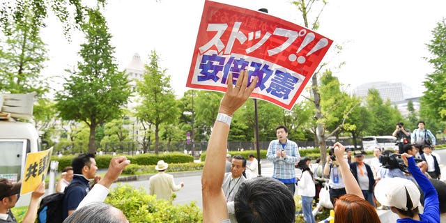 People protesting against Prime Minister Shinzo Abe's policies raise clenched fists outside parliament, background, in Tokyo Abe's ruling coalition pushed a conspiracy bill that makes it a crime to plan a crime
