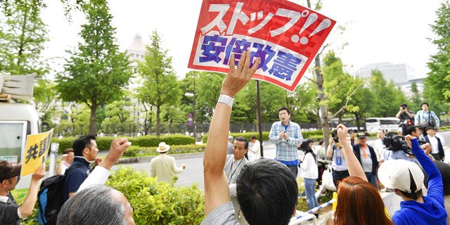 People protesting against Prime Minister Shinzo Abe's policies raise clenched fists outside parliament, background, in Tokyo Abe's ruling coalition pushed a conspiracy bill that makes it a crime to plan a crime