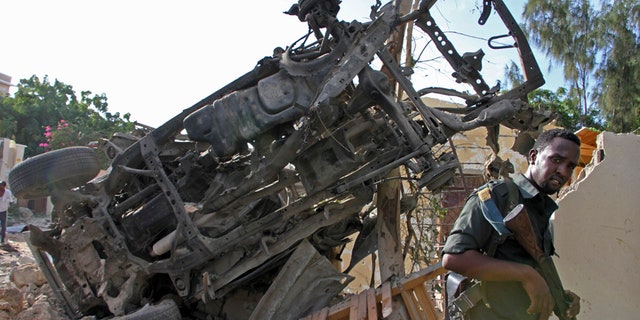 A Somali soldier stands near the wreckage from a car bomb blast and gun battle targeting a restaurant in Mogadishu, Somalia, Thursday, June 15, 2017. Somalia's security forces early Thursday morning ended a night-long siege by al-Shabab Islamic extremists at the popular "Pizza House" restaurant in the capital. (AP Photo/Farah Abdi Warsameh)