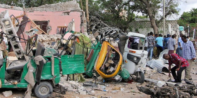 Somalis walk near destroyed vehicles at the scene of a car bomb blast and gun battle targeting a restaurant in Mogadishu, Somalia Thursday, June 15, 2017.