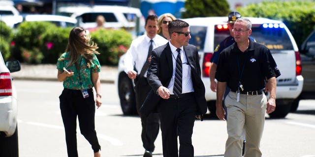 FBI Detroit spokesman Tim Wiley, center, walks over to brief the media at Bishop International Airport, Wednesday morning, June 21, 2017, in Flint, Mich. Officials evacuated the airport Wednesday, where a witness said he saw an officer bleeding from his neck and a knife nearby on the ground. Authorities say the injured officer's condition is improving. (Jake May/The Flint Journal-MLive.com via AP)