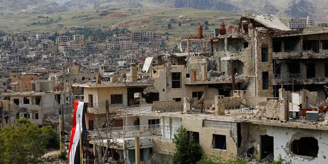 FILE - In this May 18, 2017 file photo, a Syrian National flag hangs out of a damaged building at the mountain resort town of Zabadani in the Damascus countryside, Syria.
