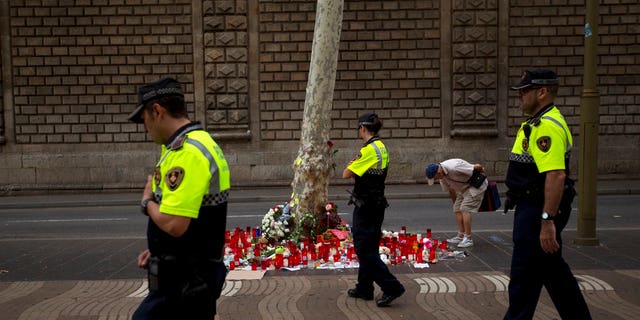 Police officers walk past candles and flowers placed on the ground after a terror attack that killed 14 people and wounded over 120 in Barcelona, Spain, Sunday, Aug. 20, 2017. (AP Photo/Emilio Morenatti)