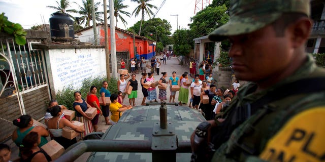 A soldier looks on as housewives stand in line for rations and water in Juchitan, Oaxaca state, Mexico, a zone heavily affected by Thursday's magnitude 8.1 earthquake, Saturday, Sept. 9, 2017.