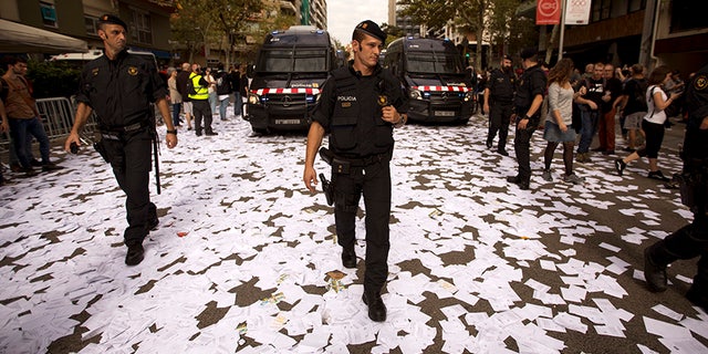 Catalan Mossos d'Esquadra officers walk a long a street covered with referendum ballots thrown by pro-independence demonstrators, during a rally in front of the Spanish Partido Popular ruling party headquarters in Barcelona, Spain, Tuesday Oct. 3, 2017. Labor unions and grassroots pro-independence groups are urging workers to hold partial or full-day strikes throughout Catalonia to protest alleged brutality by police during a referendum on the region's secession from Spain that left hundreds of people injured. (AP Photo/Emilio Morenatti)