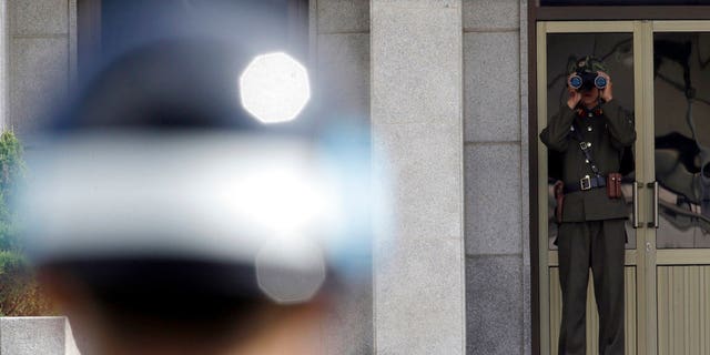 a North Korean soldier, right, looks at the south side through a pair of binoculars as a South Korean soldier, left, stands guard at the truce village of Panmunjom in the Demilitarized Zone.
