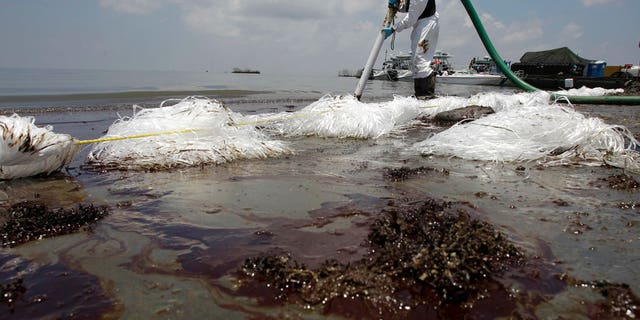 A worker uses a suction hose to remove oil washed ashore from the Deepwater Horizon spill, in Belle Terre, La., June 9, 2010.