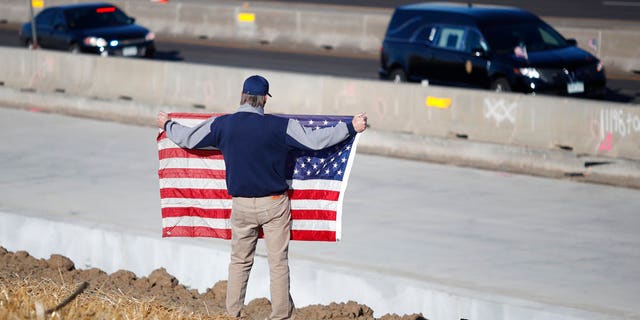 David Morgan of Highlands Ranch, Colo., holds an American flag as a procession of law enforcement vehicles accompany a hearse carrying the body of a sheriff's deputy shot and killed while responding to a domestic disturbance Sunday, Dec. 31, 2017, in Highlands Ranch, Colo.