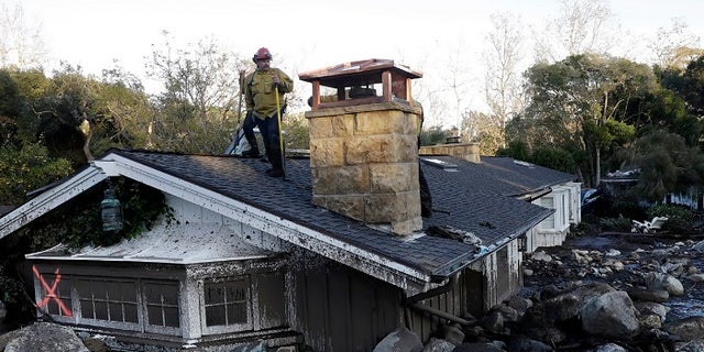 A firefighter stands on the roof of a house submerged in mud and rocks Wednesday, Jan. 10, 2018, in Montecito, Calif.