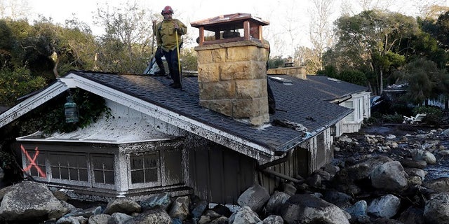 A firefighter stands on the roof of a house submerged in mud and rocks Wednesday, Jan. 10, 2018, in Montecito, Calif.