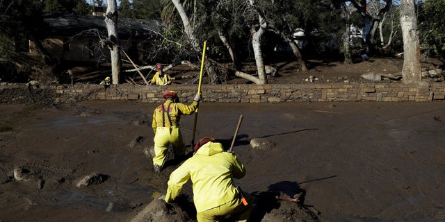 A Cal Fire search and rescue crew walks through mud near homes damaged by storms in Montecito, Calif., on Friday.